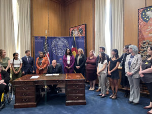 Photo of HB22-1049 bill signing, Young Advocate Kim Johnson and Policy Coordinator Sarah Staron pictured on right