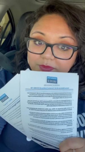 Jennifer Cardenas, a Latinx woman, sitting in the car holding up Generation Vaxxed fact sheets with information about COVID-19.